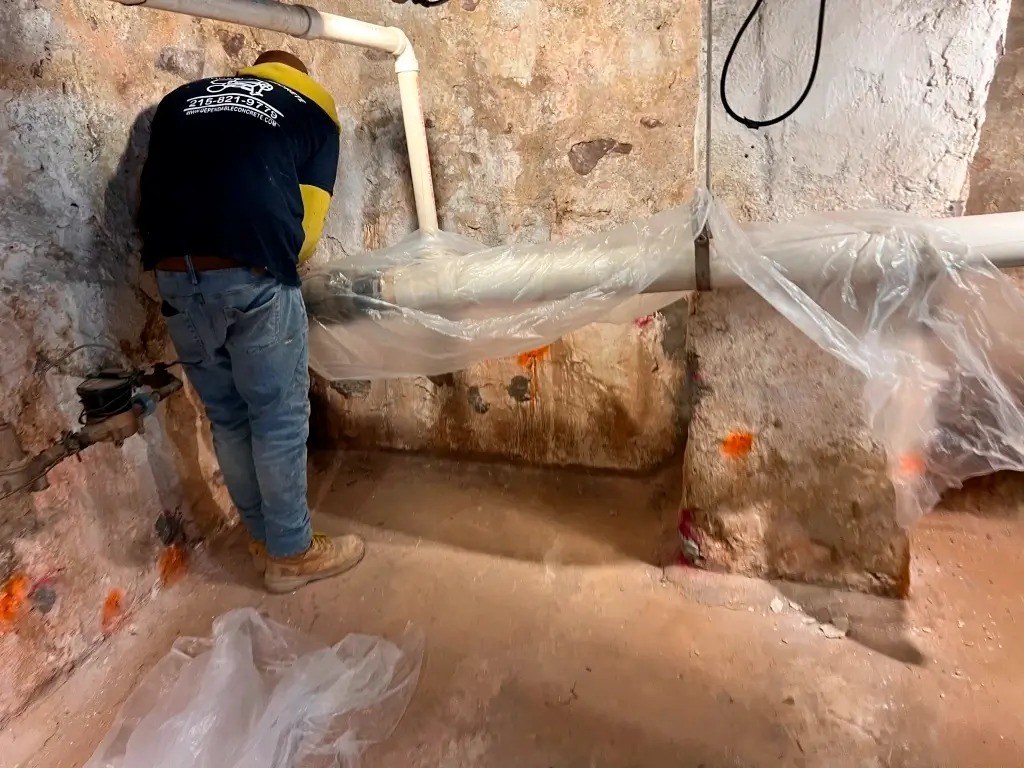 Crew preparing a basement for a new floor, with plastic sheeting and drain pipe