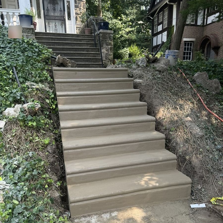 Long run of new concrete steps climbing a hillside to a stone house in Philadelphia